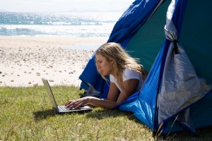 Young woman in tent using laptop at beach, side view